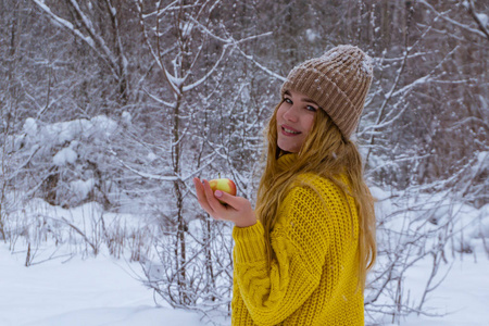 穿着暖和毛衣戴着针织帽子的女孩手里拿着一个苹果，背景是雪