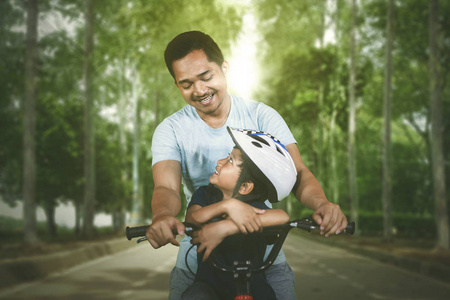 快乐的父亲和他的儿子一起骑自行车在公园的路上。 户外射击