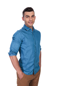 一个轻松英俊的男子，穿着蓝色衬衫，站在白色背景上，双手插在口袋里