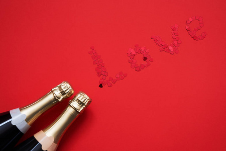 两个香槟瓶与心形纸屑形成字爱红色背景。 复制空间顶部视图。 平躺的情人节周年纪念单身庆祝概念。