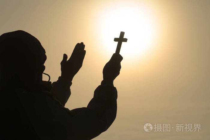 基督教男子的剪影,手中拿着十字架,祈祷上帝在阳光背景下的祝福,希望