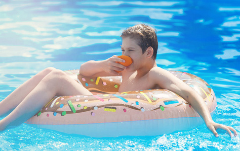 可爱的孩子男孩在有趣的充气甜甜圈浮动戒指在游泳池与橘子。 青少年学习游泳在度假村的户外游泳池里玩得很开心。 给孩子们的水玩具。 