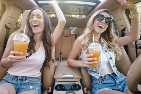 两个迷人的女人坐在车里用吸管喝新鲜果汁