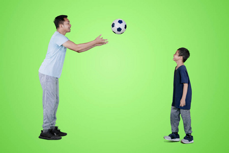 年轻人在画室里用绿色的屏幕向儿子投掷足球的照片