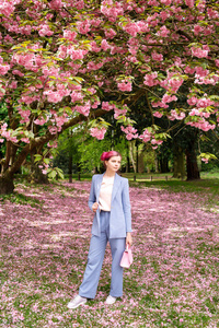 美丽的女孩，粉红色的头发，穿着一件时髦的蓝色裤子，站在五颜六色的花朵旁边。 漂亮的软模型看着相机。