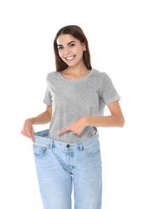 苗条的女人穿着白色背景的超大牛仔裤。 重量损失