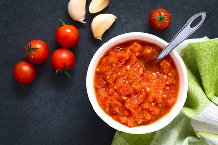 自制的意大利传统玛丽娜拉或波莫多罗番茄酱，由新鲜番茄大蒜干牛至和盐制成，放在碗里，配料放在头顶的石板上，自然光线选择性聚焦
