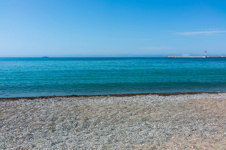 鹅卵石海滩，蓝色的大海，有灯塔的防波堤