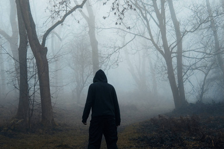 在雾蒙蒙的冬天，一个戴着兜帽的眺望着一片阴森森的森林。 一个灰色的兵变编辑。