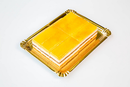白色背景上金色托盘上美丽的黄色蛋糕
