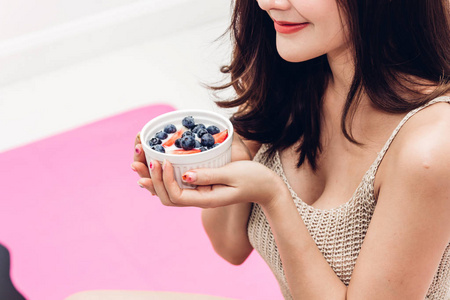 健身妇女在家里放松时，拿着酸奶和混合浆果蓝莓和草莓。健康的生活方式