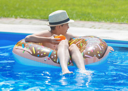 可爱的孩子男孩在有趣的充气甜甜圈浮环在游泳池与橘子。青少年学习游泳，在度假村户外游泳池玩得开心。给孩子们的水玩具。健康体育活动