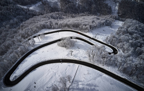 空中无人驾驶飞机看到一条弯曲的蜿蜒的道路，穿过森林，在冬天，山上覆盖着白雪