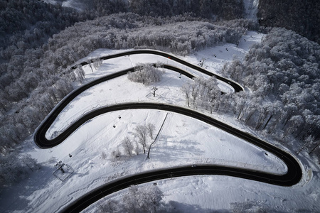 空中无人驾驶飞机看到一条弯曲的蜿蜒的道路，穿过森林，在冬天，山上覆盖着白雪