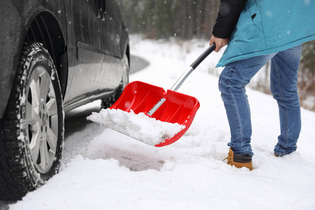 一个人在户外的被卡住的汽车附近用铲子清理积雪