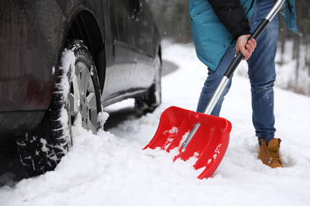 一个人在户外的被卡住的汽车附近用铲子清理积雪