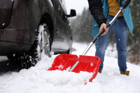 一个人在户外的被卡住的汽车附近用铲子清理积雪