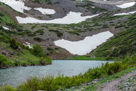 山峡。 山里的蓝色湖泊。 多云的天空雪坡。 把水融化。 湖的石岸。 水库的表面。