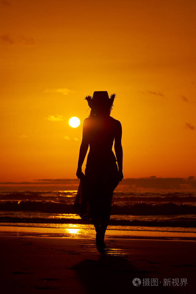 夏日夕阳下沙滩上的年轻女子剪影