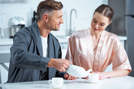 美丽微笑的成年夫妇穿长袍，在厨房喝茶