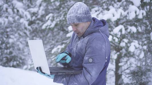 冷冻的人在冬天的森林使用笔记本电脑