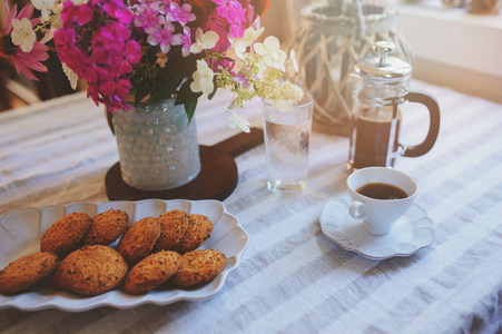在舒适的乡间别墅里吃夏季早餐。 桌子上有一束鲜花，来自自己的花园，法式印刷机，咖啡和饼干。 快乐的生活。