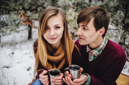 快乐的年轻夫妇在冬天的森林里野餐时喝着覆盖的葡萄酒