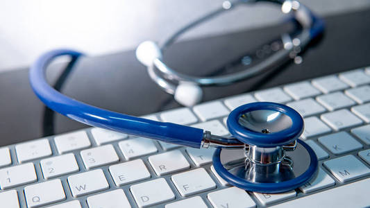 医学科学技术概念。 医生桌上白色现代键盘上的蓝色听诊器。 健康和健康背景。 全球医疗保健业务。 电脑防病毒保护