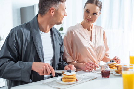 早餐时穿长袍的漂亮夫妇，厨房里有煎饼和橙汁