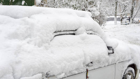 大雪后的院子。 汽车上覆盖着厚厚的一层雪。 一辆雪覆盖的豪华轿车的右侧