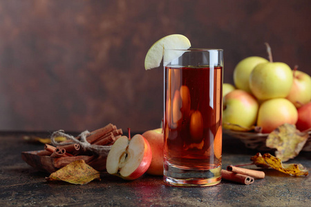 一杯苹果汁或苹果酒，加多汁的苹果和肉桂棒在厨房的桌子上。