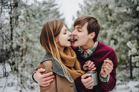 在雪地公园野餐时吃饼干和喝热茶的快乐年轻夫妇的肖像