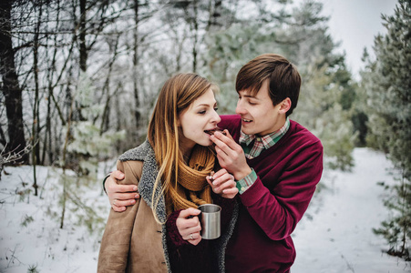 在雪地公园野餐时吃饼干和喝热茶的快乐年轻夫妇的肖像
