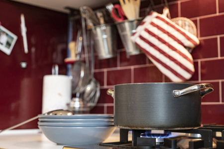 灰色炊具在煤气炉上，蒸汽释放和蓝色盘子在红色勃艮第经典厨房的一侧，背景是工具。