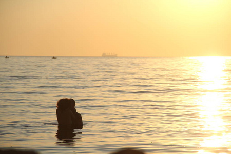 情侣在日出时亲吻水中的剪影，浪漫和爱情的概念，太阳调与软饱和过滤器。