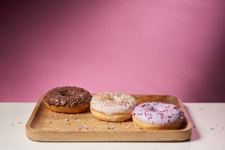 美味的釉面甜甜圈洒在粉红色背景的木切割板上