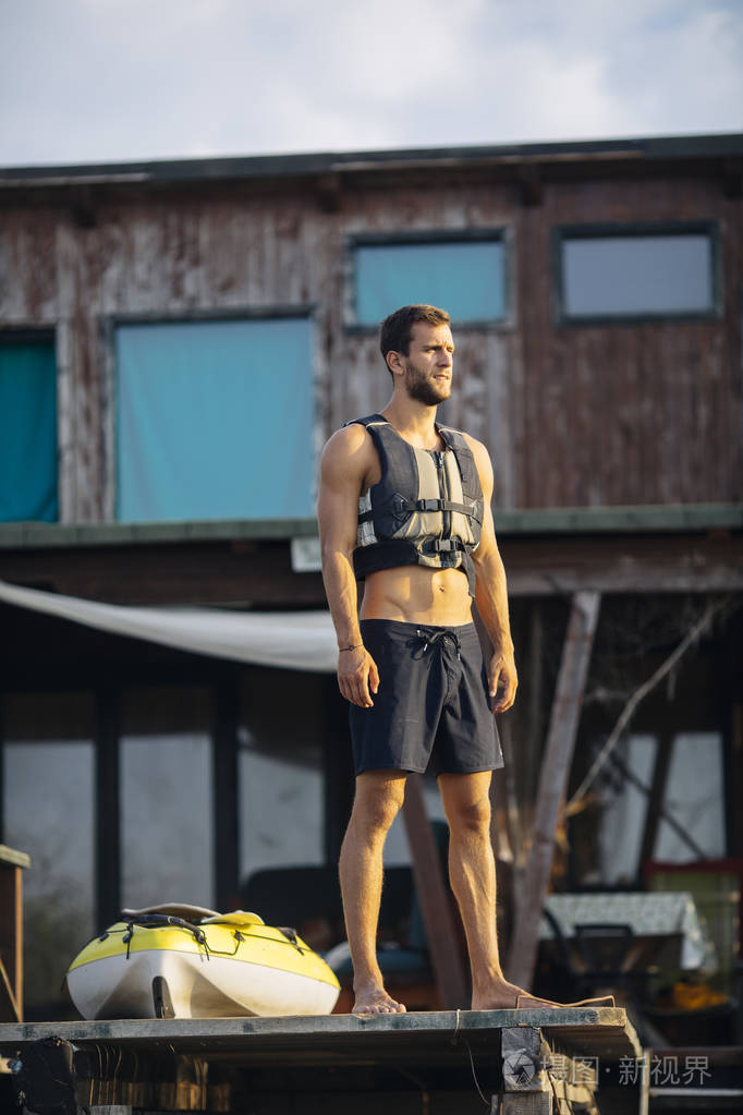 一个穿着救生衣站在木码头上的年轻白人男子。