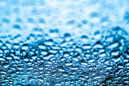 雨后玻璃窗上有宏滴的蓝色背景。 雨滴在窗户上的纹理。 宏观镜头