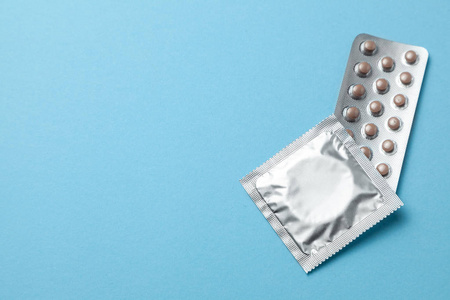在蓝色背景下, 避孕药和避孕套包。选择避孕方法避孕药或避孕套的概念。复制文本的空间