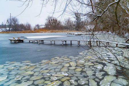 一条美丽的冰冻河流上覆盖着雪的木桥，周围环绕着农村背景的树木。 冬季的自然景观