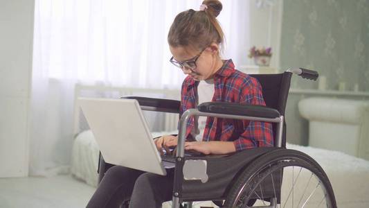 一个在轮椅上的十几岁的残疾女孩的肖像使用笔记本电脑