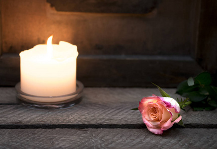 一支燃烧的蜡烛矗立在木箱上，一朵玫瑰放在黑暗的木制背景上