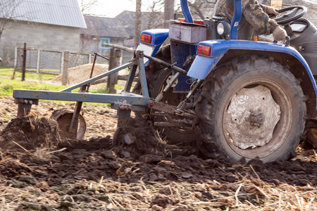 春天的田野，一位老农在蓝色的拖拉机上耕作，在春天的天空的背景下肥料