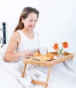 中年妇女在床上吃早餐，咖啡和羊角面包。