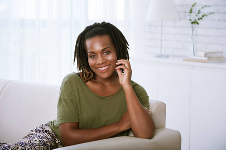 一位年轻的非裔美国人微笑的女人躺在家里的沙发上的画像