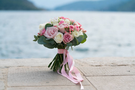 粉红白色婚礼花束站在海边的码头上