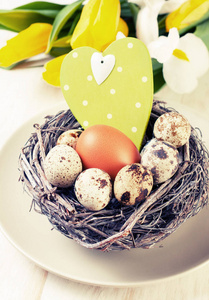复活节装饰。 木制背景下的巢郁金香中的鸡和鹌鹑蛋