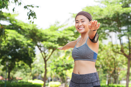 年轻快乐的亚洲女人，穿着运动服和袖章，手分开，在夏季公园训练