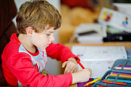 肖像的可爱快乐的学校孩子男孩在家里做家庭作业。用彩色铅笔，在屋里写字的小孩。小学和教育。刚出生的宝宝学习写字母和数字