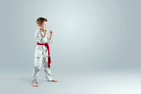 创意背景，一个穿着白色和服的孩子，站在战斗的立场上，背景很轻。武术，空手道的概念，从小运动，纪律，第一名，胜利..复制空间。
